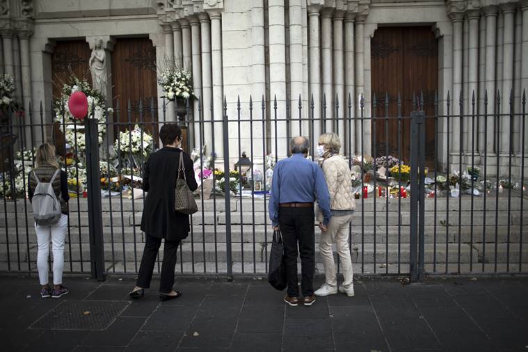 People pay respect to the victims in front of the Notre Dame church in Nice, France, Friday, Oct. 30, 2020. A new suspect is in custody in the investigation into a gruesome attack by a Tunisian man who killed three people in a French church. France heightened its security alert amid religious and geopolitical tensions around cartoons mocking the Muslim prophet. (AP Photo/Daniel Cole)