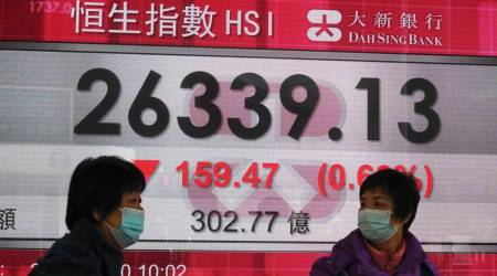 People wearing face masks walk past a bank's electronic board showing the Hong Kong share index in Hong Kong, Monday, Dec. 21, 2020. (AP Photo/Kin Cheung)