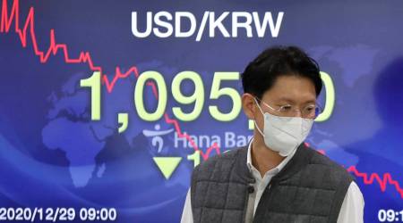 A currency trader walks by the screen showing the foreign exchange rate between US dollar and South Korean won at the foreign exchange dealing room in Seoul, South Korea, Tuesday, Dec. 29, 2020. (AP Photo/Lee Jin-man)