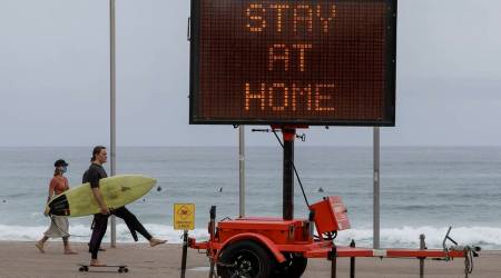 A surfer carries his board as he skates along the beach front at Manly on the northern beaches in Sydney (AP Photo/Mark Baker)