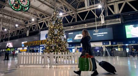 FILE - In this Sunday Dec. 20, 2020 file photo a woman pulls a suitcase past the Christmas tree on the concourse of Waterloo Station in central London, (Victoria Jones/PA via AP, File)