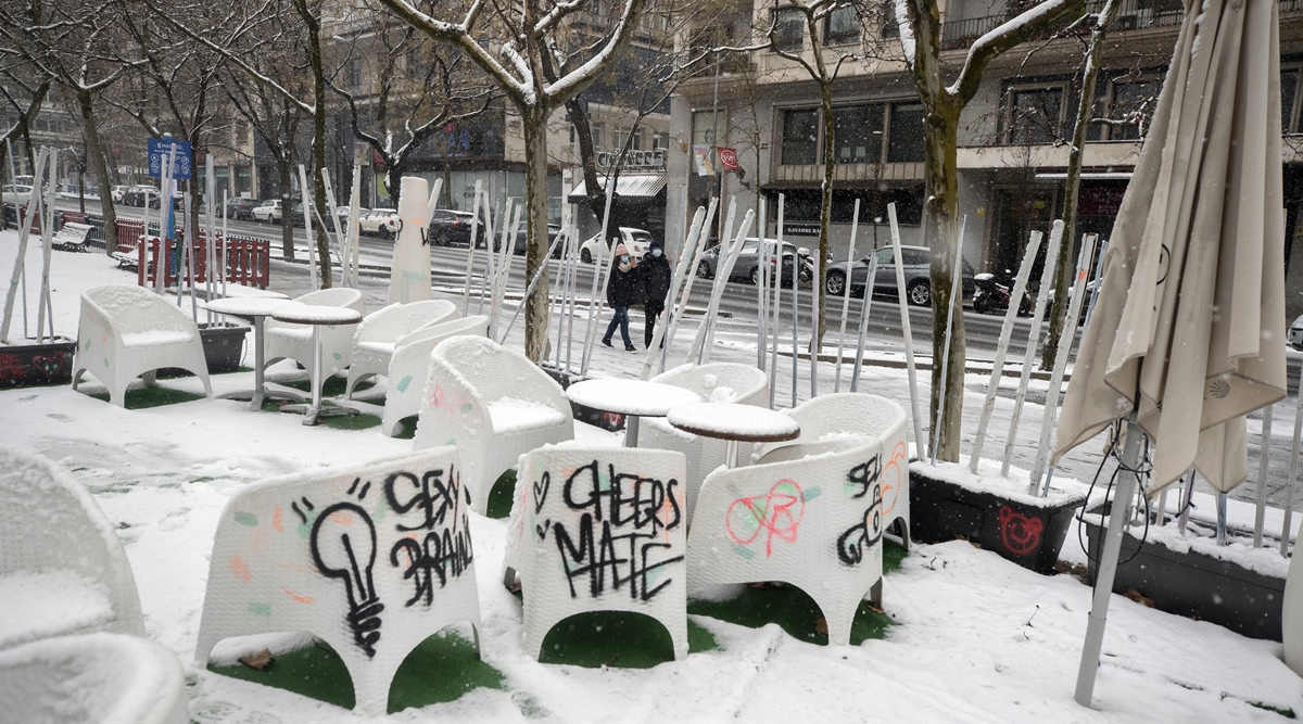 A couple walk past a terrace bar with tables and chairs covered with snowduring a snowfall in Madrid, Spain, Friday, Jan. 8, 2021. (AP Photo/Paul White)