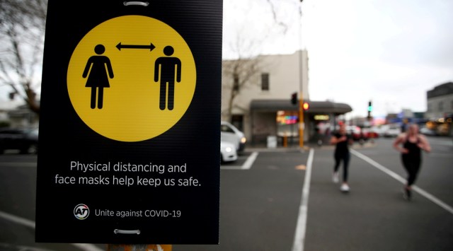 FILE PHOTO: People jog past a social distancing sign on the first day of New Zealand's new coronavirus disease (COVID-19) safety measure that mandates wearing of a mask on public transport, in Auckland, New Zealand, August 31, 2020.  REUTERS/Fiona Goodall/File Photo