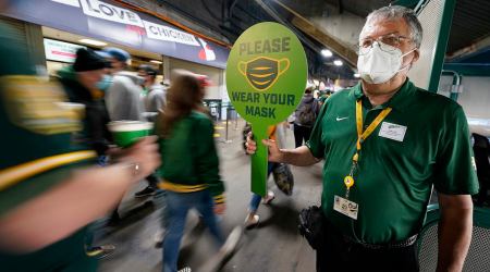 John Abercrombie, an usher for the Oakland Athletics, holds up a sign advising people to wear masks, prior to a baseball game between the Ahletics and the Houston Astros on Friday, April 2, 2021, in Oakland, Calif. (AP Photo/Tony Avelar)
