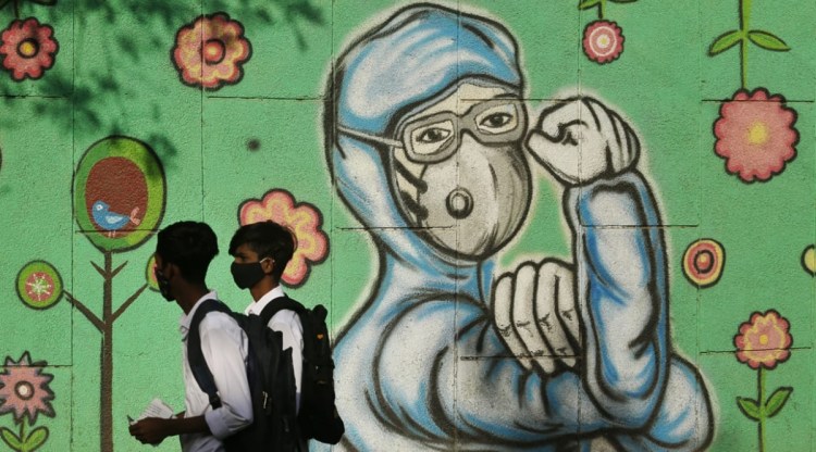 People walk past a wall graffiti in New Delhi showcasing doctors fighting against Covid-19. (Express Photo: Praveen Khanna)