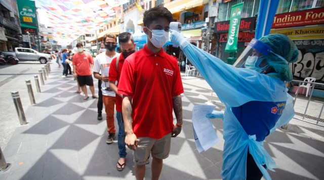 A health worker checks the temperature of a man falling in line for a COVID-19 swab test in Khaosan Road in Bangkok, Thailand Wednesday, April 14, 2021. Thailand recorded more than 1,000 COVID-19 infections on Wednesday, setting a daily record and adding pressure on the government to do more to control the country's spiking transmission rates. (AP Photo/Somchai Chanjirakitti)