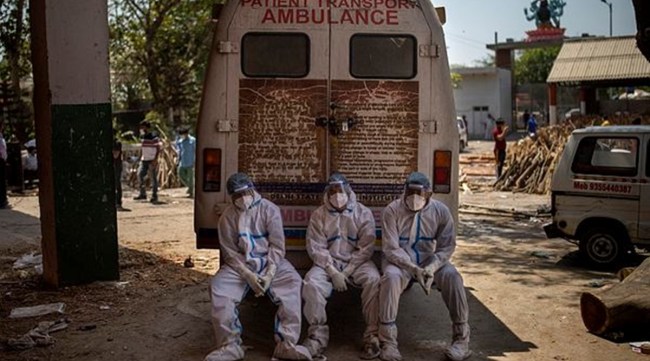 Exhausted workers who carried the dead for cremation sit on the rear step of an ambulance in New Delhi, India. (AP Photo)