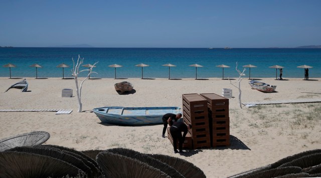 Workers arrange sunbeds as others install umbrellas at Plaka beach on the Aegean island of Naxos, Greece. (Photo: AP)