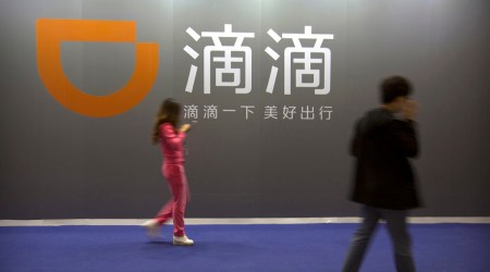 In this April 27, 2017, file photo, visitors walk past a sign for Chinese ride-hailing service Didi Chuxing at the Global Mobile Internet Conference (GMIC) in Beijing. Chinese ride-hailing service Didi says it lost $5.5 billion over the past three years ahead of its US stock market debut Wednesday, June 30, 2021, but it's highlighting its global reach and investments in developing electric and self-driving cars. (AP Photo)
