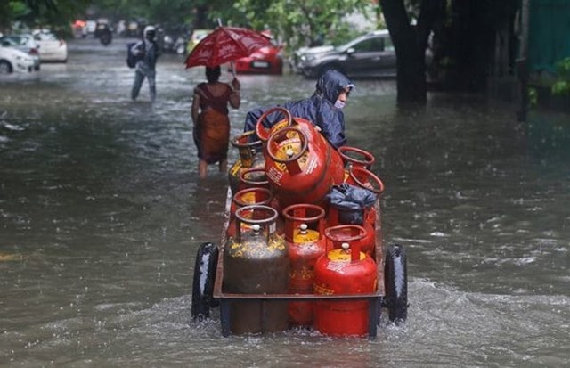 A man pushes his hand cart loaded with cooking gas cylinders through a flooded street during heavy rains in Mumbai, India, Saturday, June 12, 2021. The city was battered with heavy rainfall that continued for days. (AP Photo)