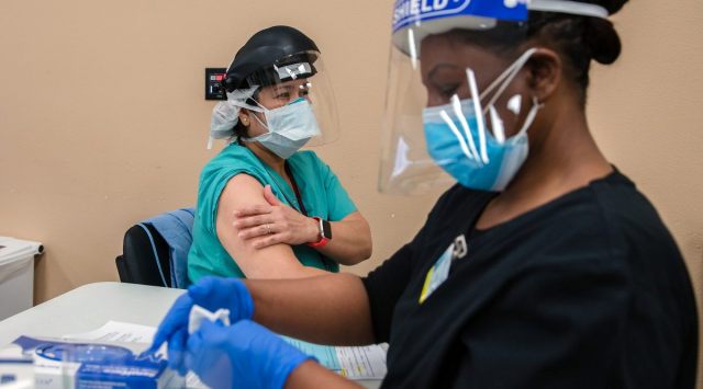 A health care worker prepares to administer a COVID-19 vaccine to a nurse at Providence St. Mary Medical Center in Apple Valley, Calif., Dec. 17, 2020. (The New York Times)