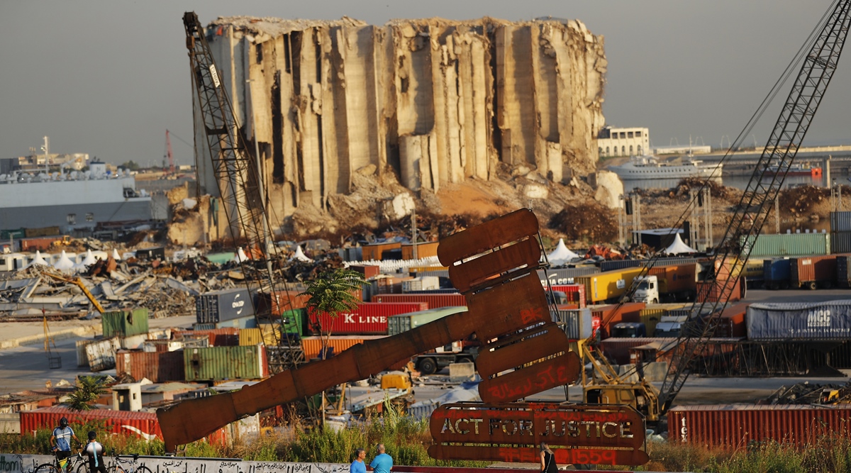 People pass next of a justice symbol monument that sits in front of towering grain silos gutted in the massive August 2020 explosion at the Beirut port that claimed the lives of more than 200 people, in Beirut, Lebanon, Wednesday, Aug. 4, 2021. (AP)