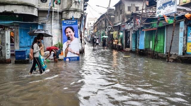 Pedestrians walk past a banner of West Bengal CM Mamata Banerjee on a waterlogged road during heavy rain in Kolkata | PTI/file