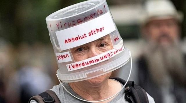 A demonstrator walks through Berlin-Charlottenburg with a plastic bucket placed on his head reading 'Absolutely safe against the stupidity virus', in Berlin, Sunday. (AP)