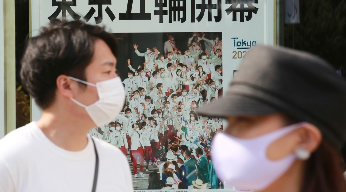People wearing face masks to protect against the spread of the coronavirus walk past an extra paper reporting Tokyo Olympics start in Tokyo Saturday, July 24, 2021. (AP Photo/Koji Sasahara)