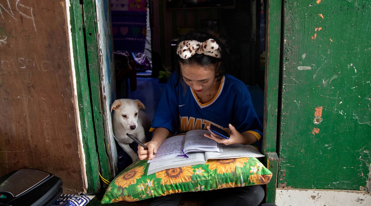 Annie Sabino, 16, a grade 9 student, completes her school work next to her dog, while tending to her family's sidewalk eatery beside their home, as schools remain closed during the coronavirus disease (Covid-19) outbreak, in Manila, Philippines, January 6, 2021 | Reuters/File Photo