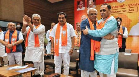 New Gujarat CM Bhupendra Patel (second from right) is greeted by outgoing CM Vijay Rupani in Gandhinagar Sunday. (Express photo by Nirmal Harindran)