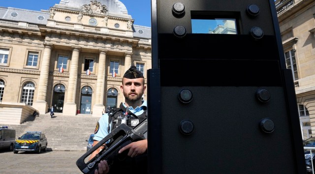 A police officer stands behind a shield outside the Paris courthouse. AP