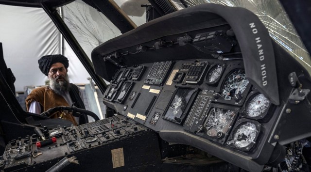 A damaged US Black Hawk helicopter, disabled by withdrawing US forces before it was left behind, is examined by a Taliban fighter at the airport in Kabul on Aug. 31, 2021. (Victor J. Blue/The New York Times)