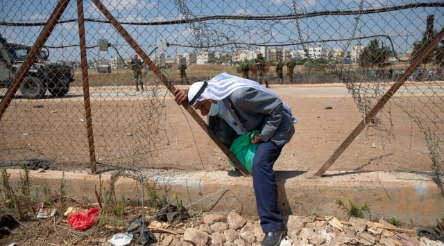 Israeli soldiers watch as a Palestinian laborer crosses through a damaged section of the Israeli separation fence, returning home after a days work in Israel, in the West Bank village of Jalameh. (AP)