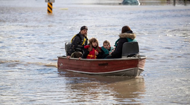 A woman and children who were stranded by high water due to flooding are rescued by a volunteer operating a boat in Abbotsford, British Columbia (AP)