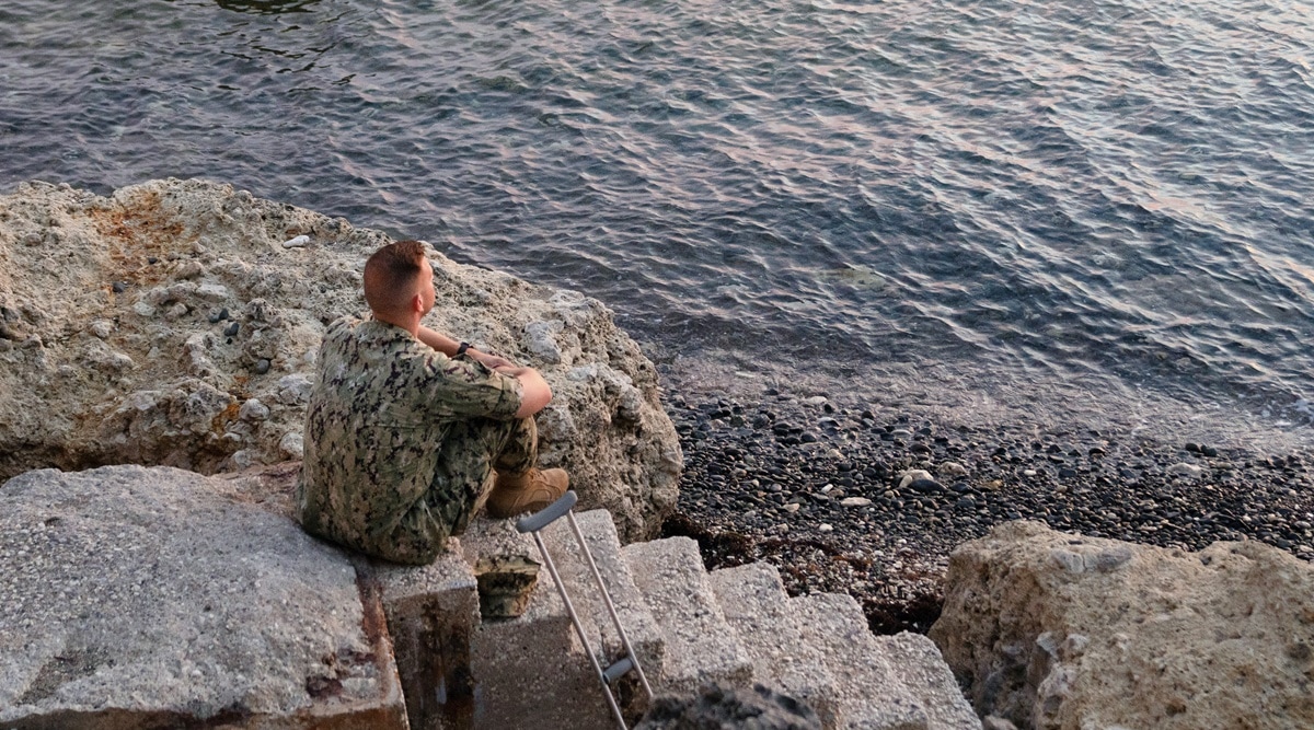 A Naval officer watches the sunset from Glass Beach at Naval Station Guantanamo Bay in Cuba, on Sept. 22, 2021. The base has beaches, parks with barbecue grills and pleasure boats to rent for sailing and fishing excursions.  (Erin Schaff/The New York Times)
