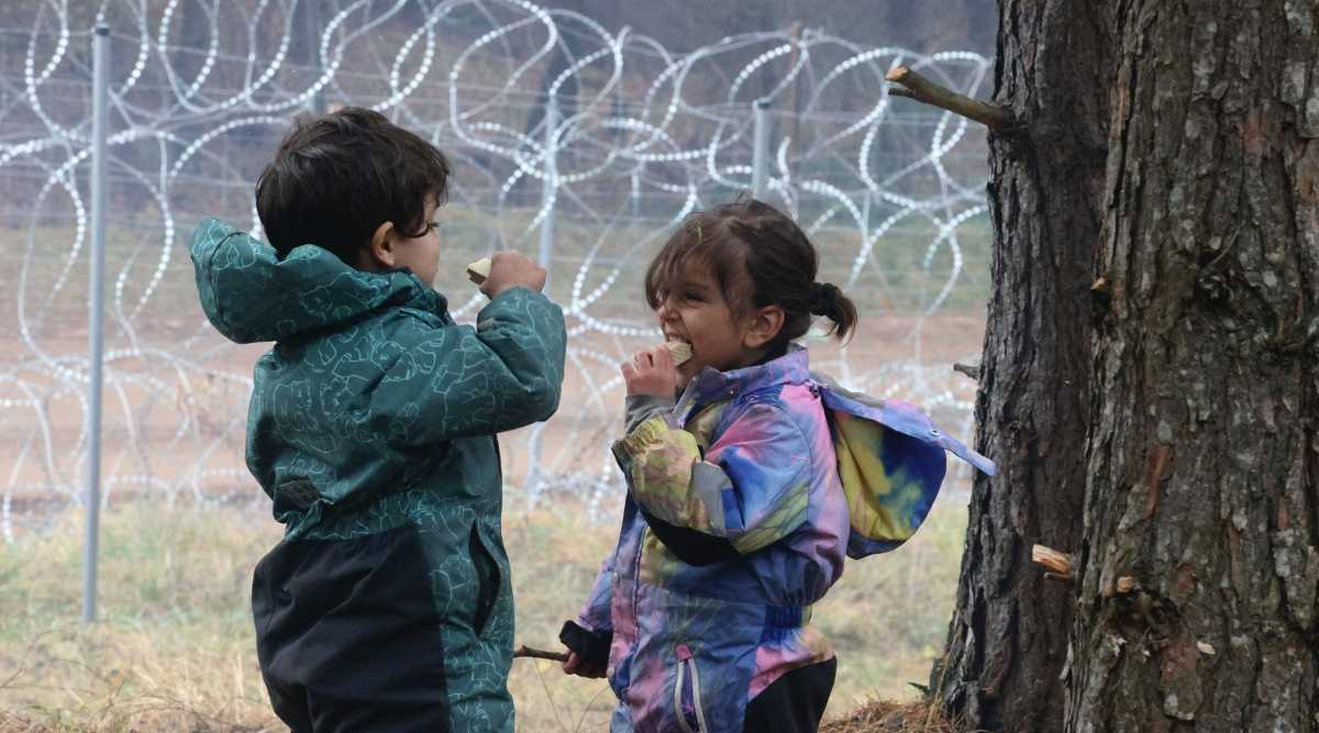 Migrant children eat near the barbed wire fence as other migrants gather at the Belarus-Poland border near Grodno, Belarus, Saturday, Nov. 13, 2021. A large number of migrants are in a makeshift camp on the Belarusian side of the border in frigid conditions. Belarusian state news agency Belta reported that Lukashenko on Saturday ordered the military to set up tents at the border where food and other humanitarian aid can be gathered and distributed to the migrants. (Photo: BelTA pool via AP)
