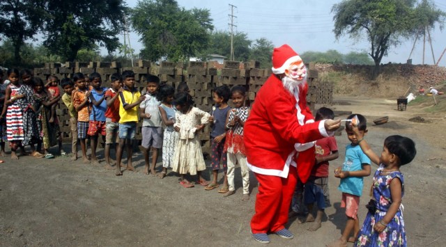 A man dressed as Santa Claus brings food for children of brick kiln workers in Pimpalas area of Kalyan on Thursday. (Express Photo by Deepak Joshi )