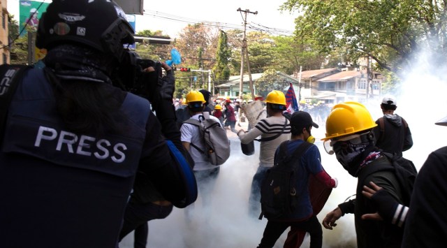A photographer wearing a protective vest with a 'press' sign at the back films an anti-military government protest being dispersed with tear gas by security forces in Sanchaung township in Yangon, Myanmar on March 3, 2021. (AP Photo)