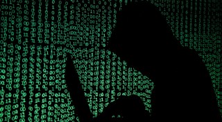 Hooded man holds laptop computer as cyber code is projected on him in this illustration picture.