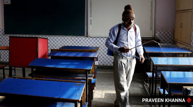 A worker sanitizes the classroom of a school after the Delhi government allowed schools to reopen for classes 9 to 12 from February 7. (Express photo by Praveen Khanna)