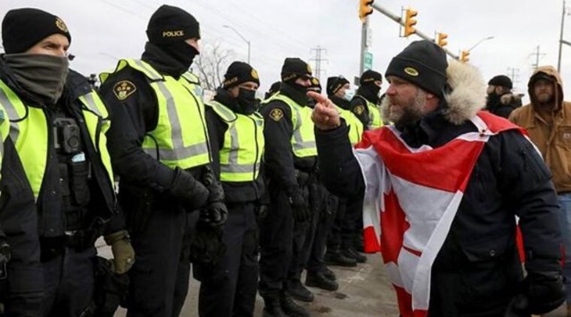 A protester gestures towards police officers, who stand guard on a street after Windsor Police said that they are starting to enforce a court order to clear truckers and supporters who have been protesting against coronavirus disease (COVID-19) vaccine mandates by blocking access to the Ambassador Bridge, which connects Detroit and Windsor, in Windsor, Ontario, Canada. (Reuters)