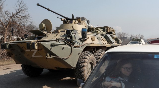 A refugee waits in a car as an armoured personnel carrier of pro-Russian troops drives out of a checkpoint in the course of Ukraine-Russia conflict in the besieged southern port city of Mariupol, Ukraine. (Reuters)