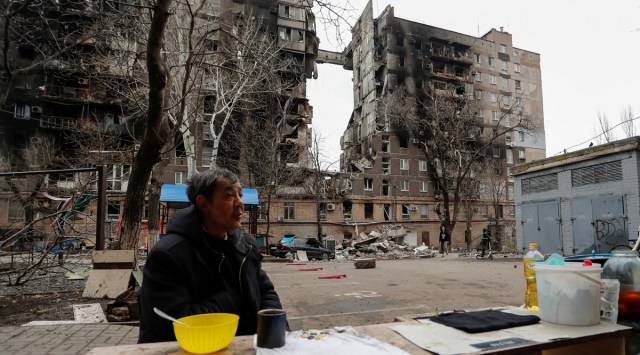 A local resident sits next to a fire in a courtyard outside a building damaged during Ukraine-Russia conflict in the southern port city of Mariupol, Ukraine April 14, 2022. (Reuters)
