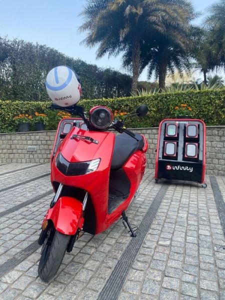 Uma scooter Bounce de cor vermelha e uma estação de troca de baterias. 