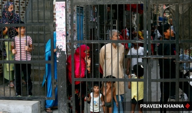 Locals stand behind gates of their houses while the investigation team probe the site the where clashes took place two communities on Saturday, at Jahangirpuri in New Delhi on Monday. 