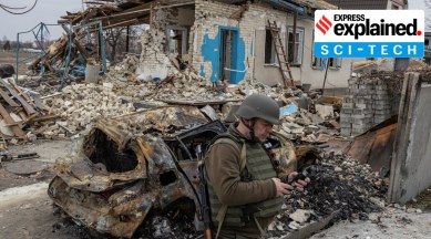 A Ukrainian serviceman checks his mobile phone in front of a destroyed house in the village of Krasylivka outside Kyiv on March 26, 2022. (Reuters Photo: Marko Djurica)