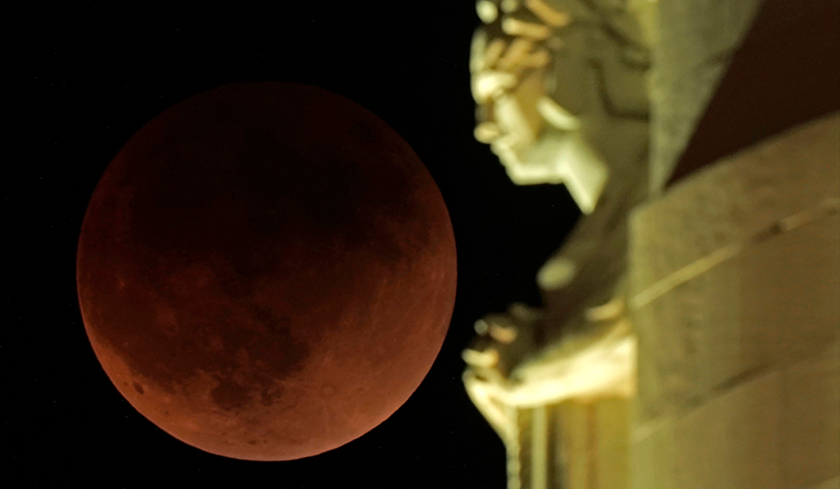A lunar eclipse covers the moon as it rises beyond a statue 