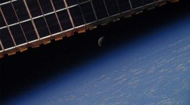 Image shows the lunar eclipse framed by the solar panels of the international space station above and the earth below it.