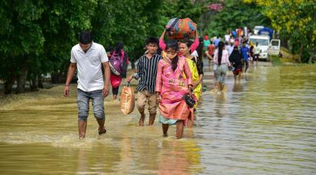 People wade through a flooded road after rain at a village in Assam’s Nagaon district on Tuesday. (PTI)