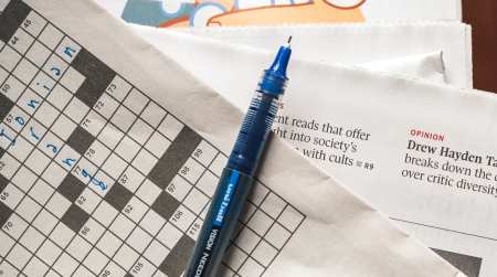 Blue pen rests on a newspaper that has a partially filled out crossword puzzle