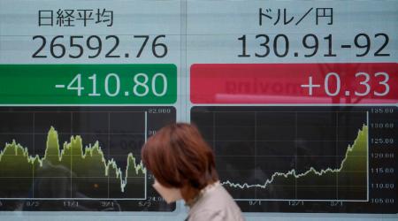 A woman wearing a protective mask walks in front of an electronic stock board showing Japan's Nikkei 225 index and Japanese yen and U.S. dollar exchange rate at a securities firm Monday, May 9, 2022, in Tokyo. (AP Photo)