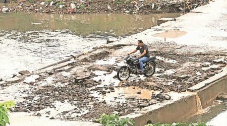 A motorcyclist negotiates a road stretch damaged by heavy rain, in Mota Mava area of Rajkot city Saturday. (Express Photo)