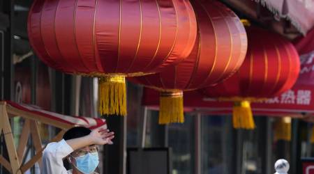 A man wearing a mask rests in the shade near Chinese lanterns, Monday, July 18, 2022, in Beijing. (AP Photo)
