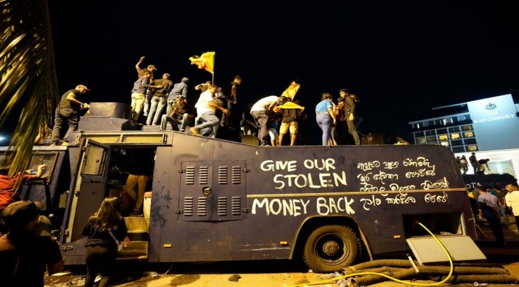 Protesters stand on a vandalised police water canon truck and shout slogans at the entrance to presidents official residence in Colombo, Sri Lanka, July 9. (AP)