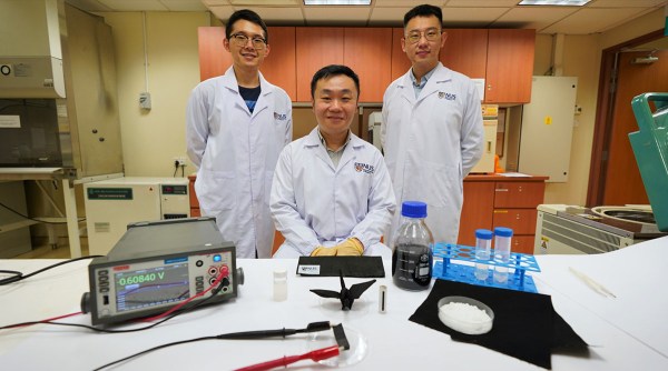 Three scientists stand in front of a device that generates electricity from moisture and the substances they use to build it