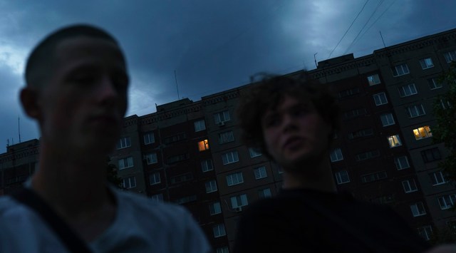 The lights in just a few windows illuminate an otherwise dark apartment block as Roman Kovalenko, 19, left, visits his friend, Oleksandr Pruzhyna, 18, right, in Kramatorsk, Donetsk region, eastern Ukraine (Source: AP)