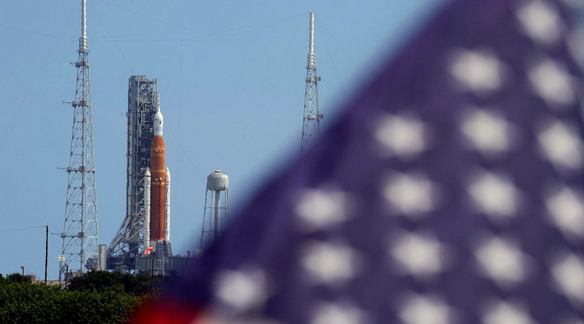 An American flag flies in the breeze as NASA's new moon rocket sits on Launch Pad 39-B after being scrubbed at the Kennedy Space Center
