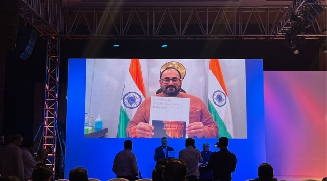 Rajeev Chandrashekhar on a projector screen hlding up paper that says "Building an Indian Quantum industry"