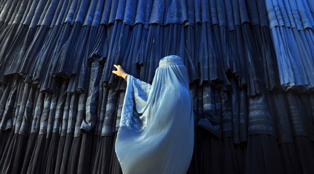 A woman clad in a burqa looks at other pieces of Afghanistan's traditional, all-encompassing dress at a store in Mazar-i Sharif, north of Kabul, Afghanistan, on Sept. 10, 2015. The Taliban announced they have arrested and will soon sentence an Afghan woman who appeared in a video on social media on Aug.  30, 2022, and said a senior Taliban official forced her into marriage and raped her repeatedly. (AP Photo)